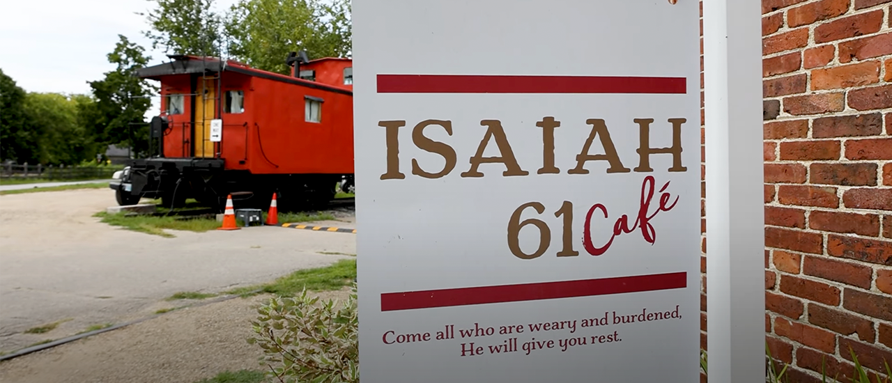 Photo of Isaiah 61 Cafe sign with train caboose in the back.